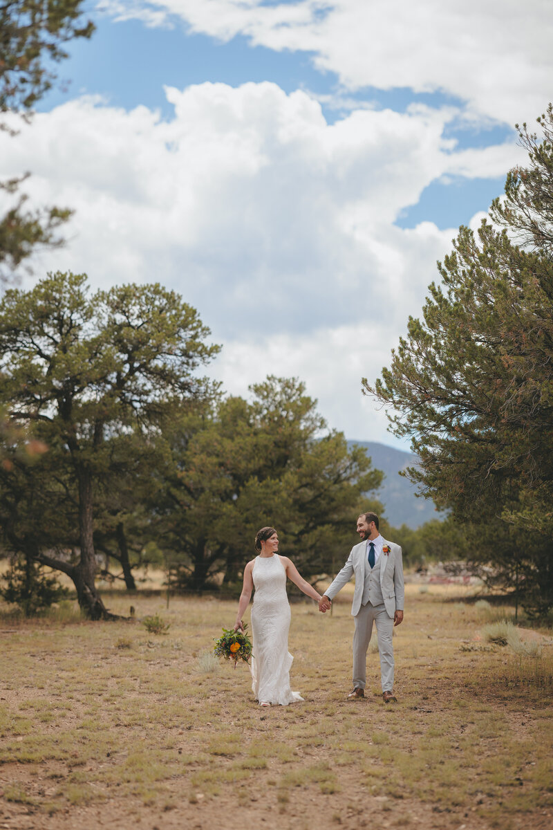 A bride and groom walking through a clearing in the Colorado mountains after their wedding ceremony