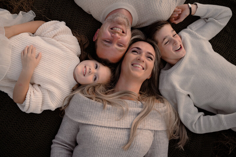Gezin van vier ligt in het gras en kijkt naar de lucht tijdens een gezinsshoot in de omgeving van Apeldoorn door Joenne Bokhorst Fotografie