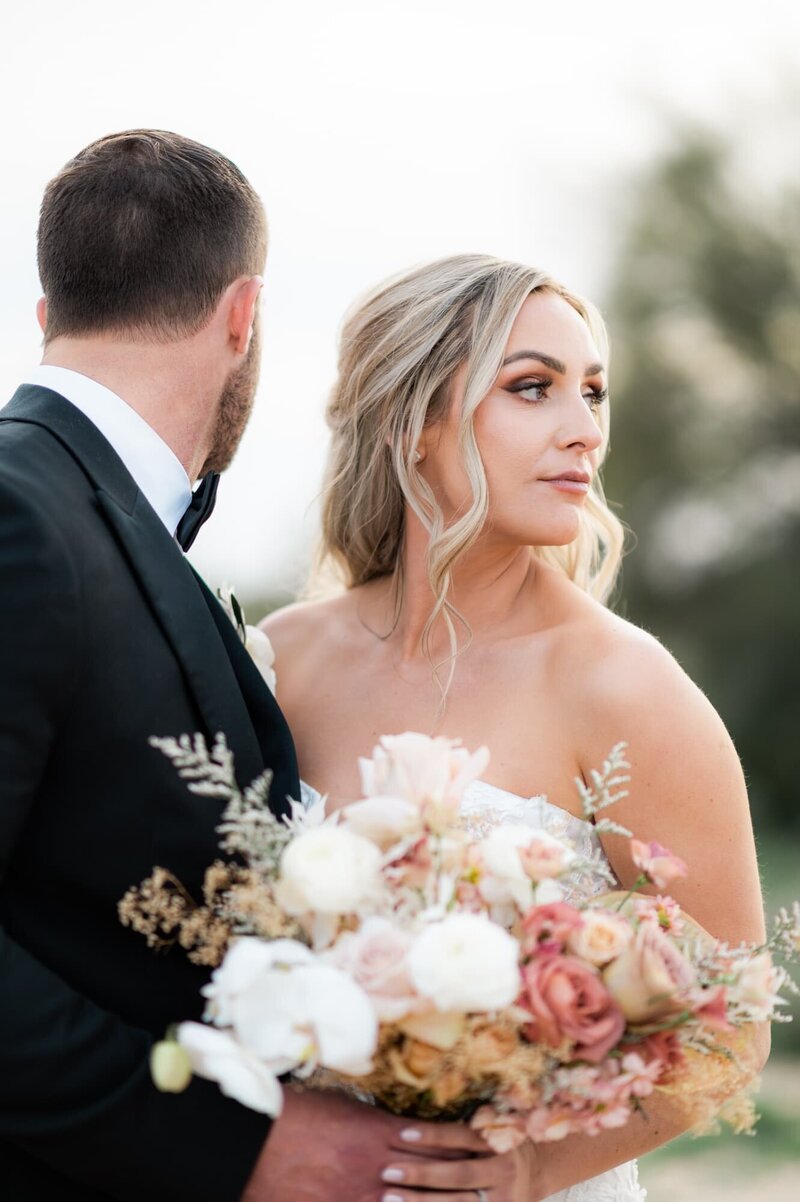 Bride looking off into the distance while holding bouquet and next to groom