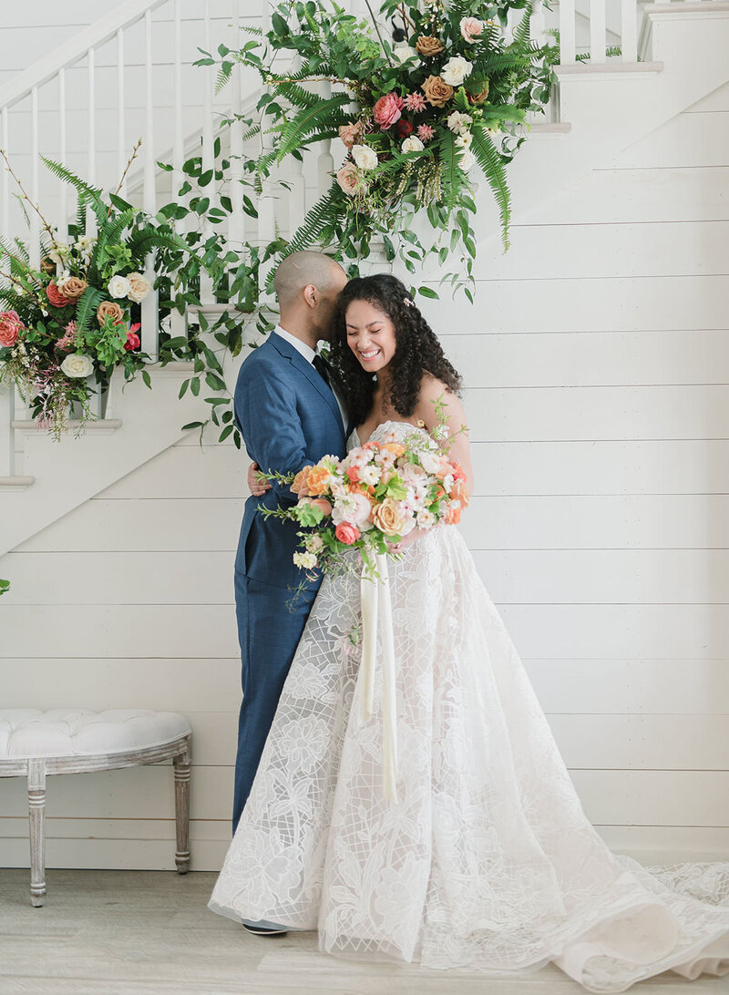 Groom embraces his bride holding floral bouquet on their wedding day