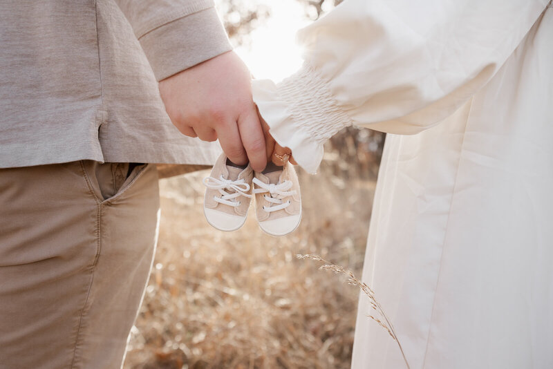 Maternity announcement image of parents hands holding a pair of baby shoes. 