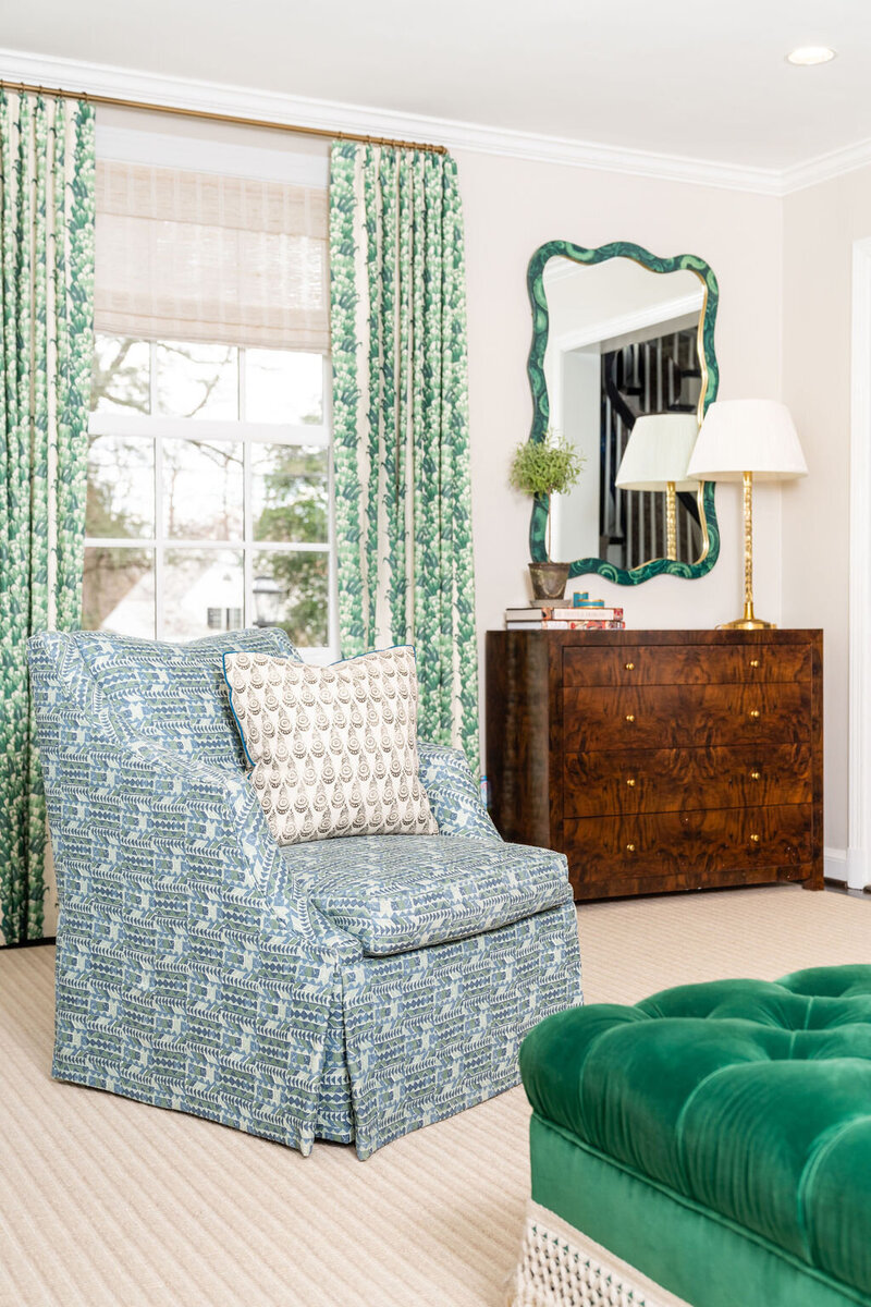 Bold living room with green velvet ottoman, blue patterned lounge chair with green floral curtains and brown dresser