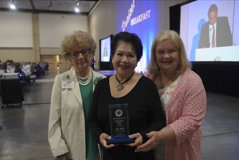 Nita Tin holding the 2023 Lydia Award plaque at Scenic City Women’s Network event in Chattanooga, Tennessee. She stands in a black dress and pearls with two women beside her, smiling with arms around her in congratulation.