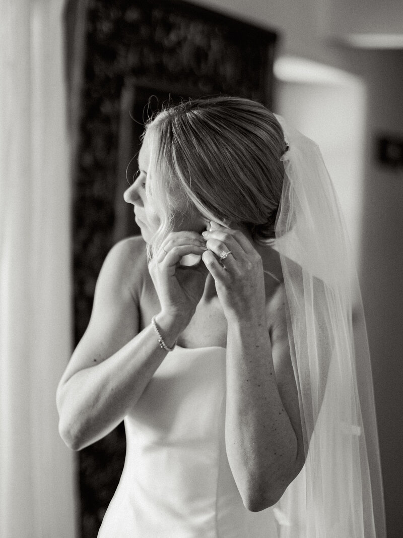 Black and white photo of bride putting on her earrings