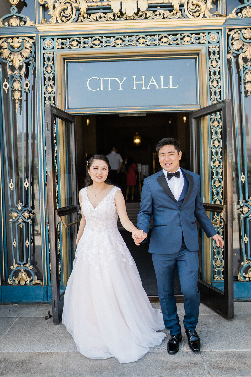 bride and groom hold hands outside san francisco city hall