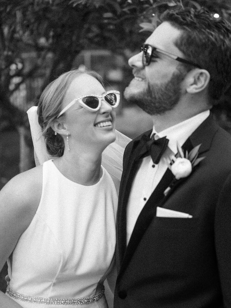 black and white photo of bride and groom laughing with sunglasses