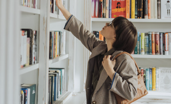 A girl reach for a book in a library. 