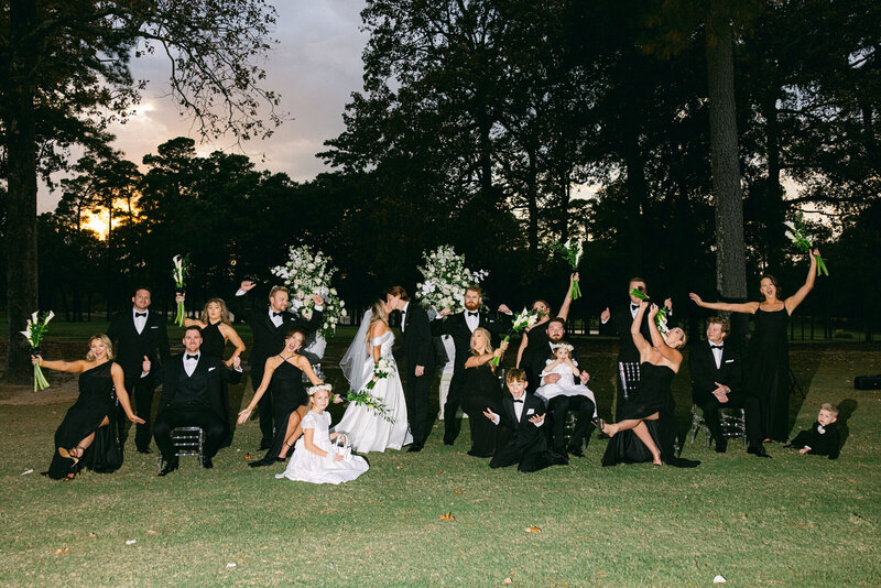 photo of a full bridal party celebrating while the married couple kiss in the middle of the group with the sun setting behind them