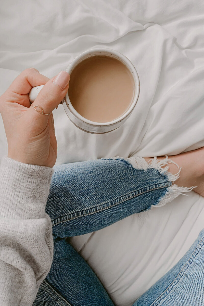 Hand holding a mug of coffee above her legs