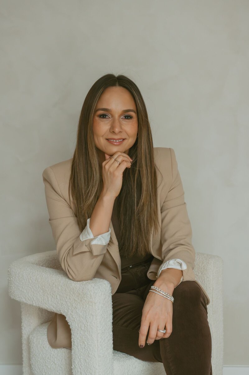 Hospitality interior designer in beige blazer with thoughtful expression, ready to transform luxury hotel and restaurant spaces near me.