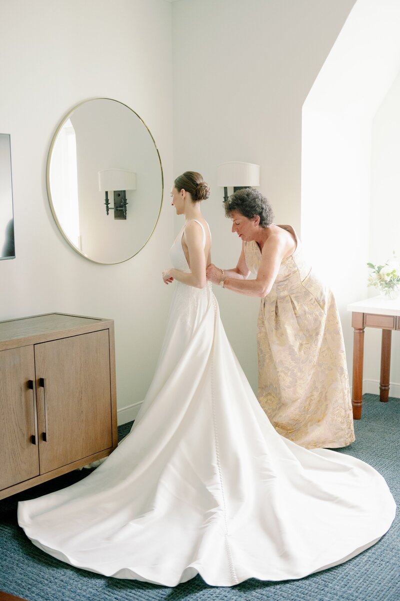 a woman helping a bride fasten her wedding dress