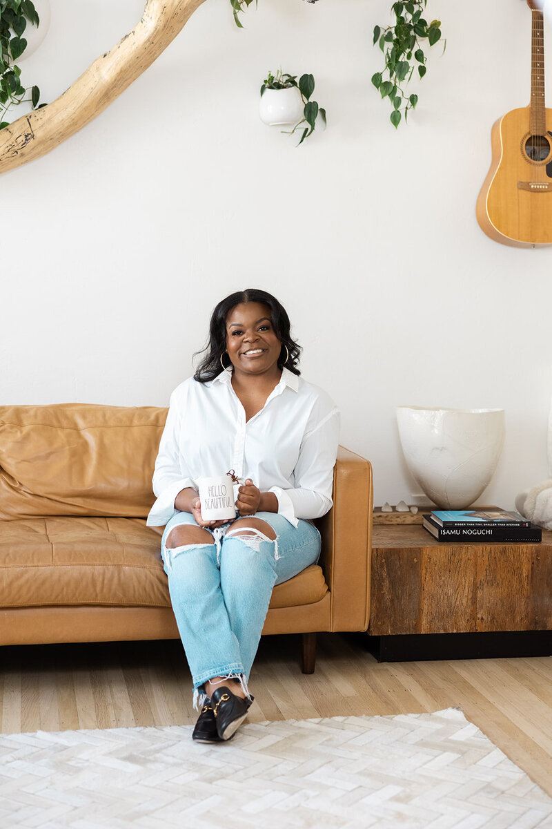 Realtor sitting on a tan couch holding a coffee mug for her san francisco brand photography shoot.