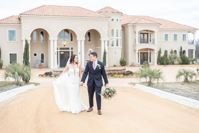 bride and groom walking and holding hands in front of mediterranean mansion
