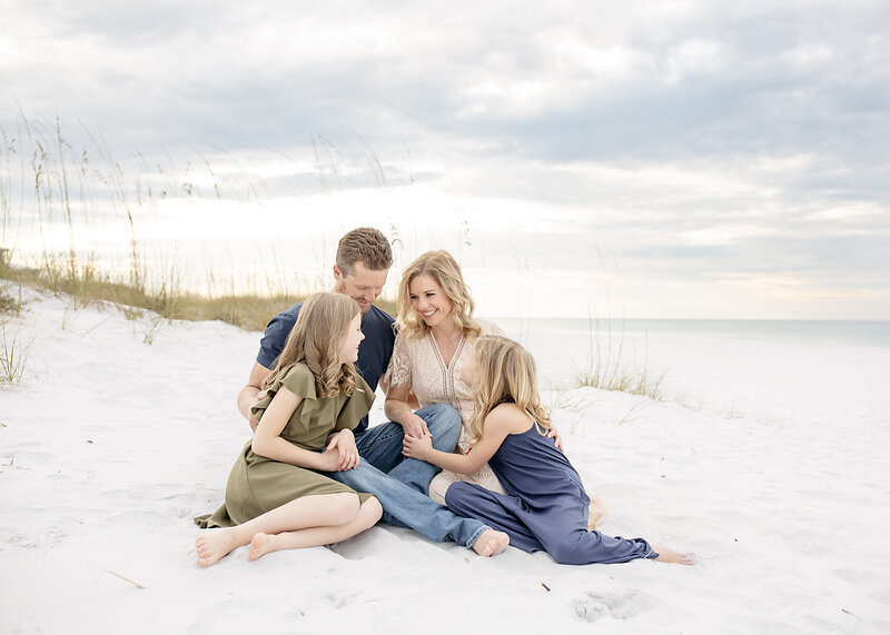 A family is sitting on the beach in 30a smiling at each other