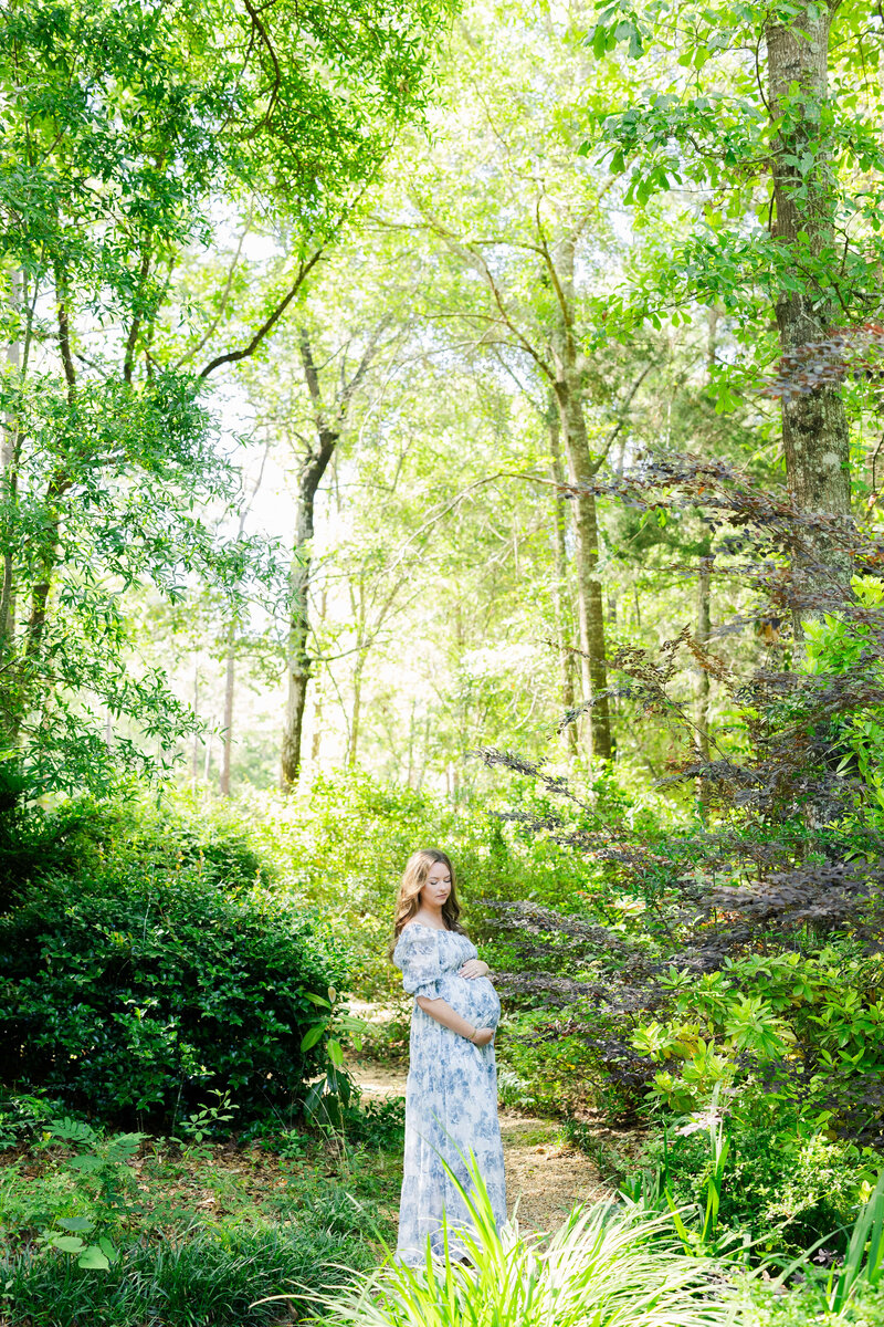 Woman standing in dothan alabama woods while holding pregnant belly for maternity photography session