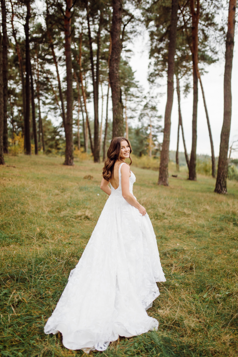 A serene image of a bride walking gracefully among lush green grass and tall trees, exuding tranquility and natural beauty on her wedding day.