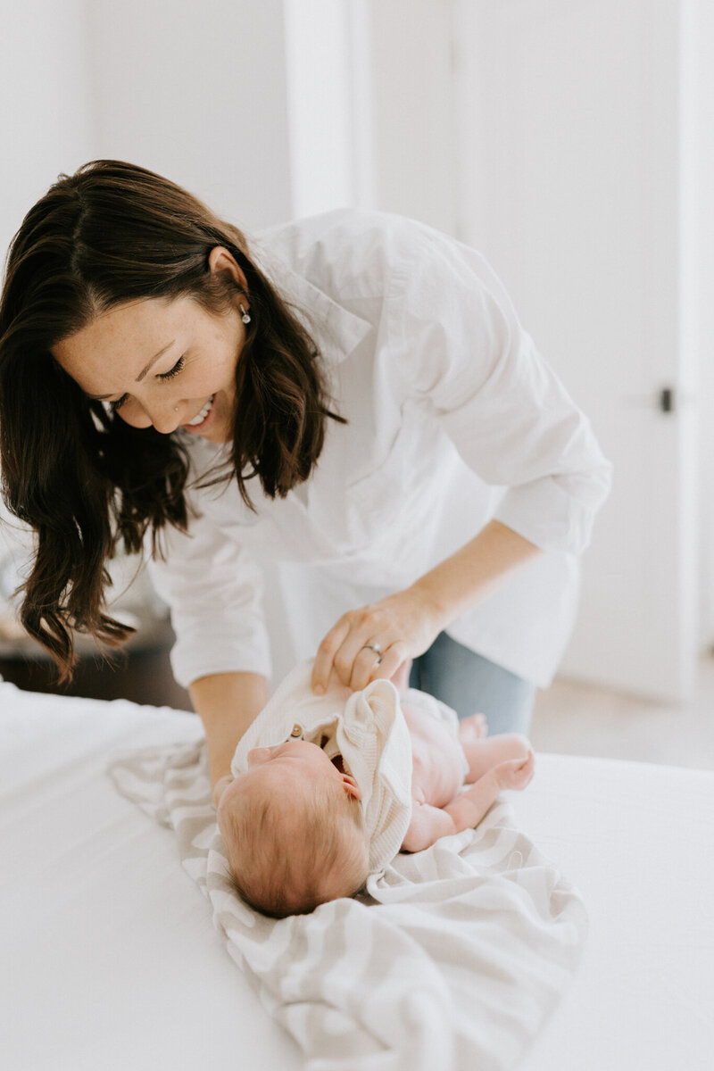 A new mom smiles while swaddling her new baby boy for this West Lafayette newborn photography session by Vanessa Stoller.