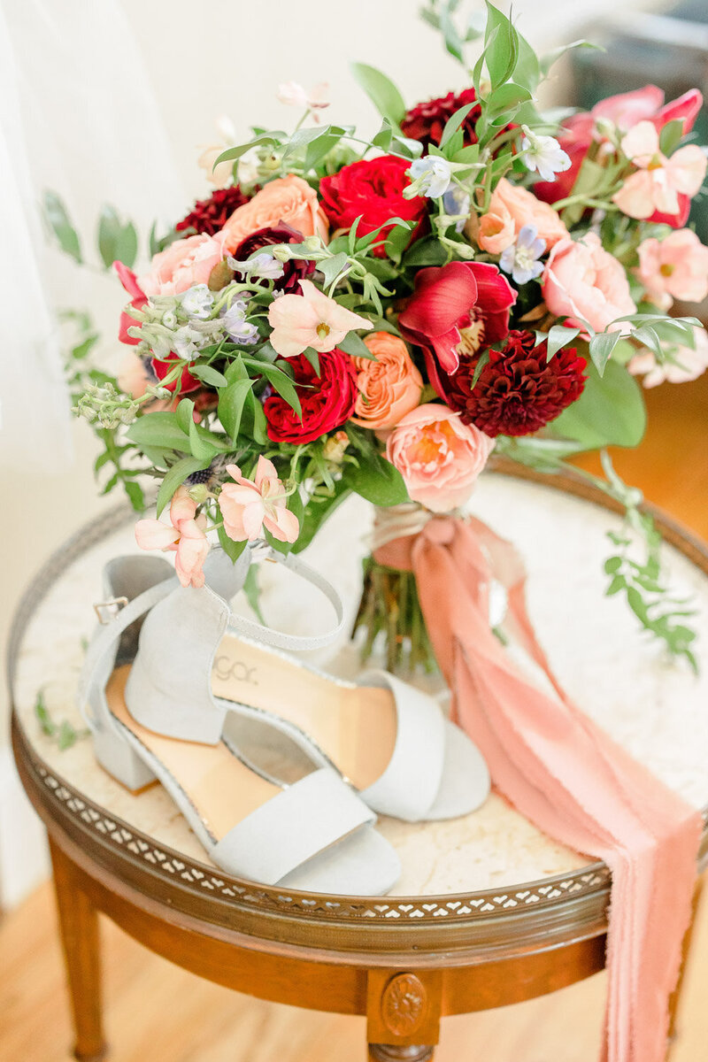 Bridal bouquet with red and peach flowers beside shoes