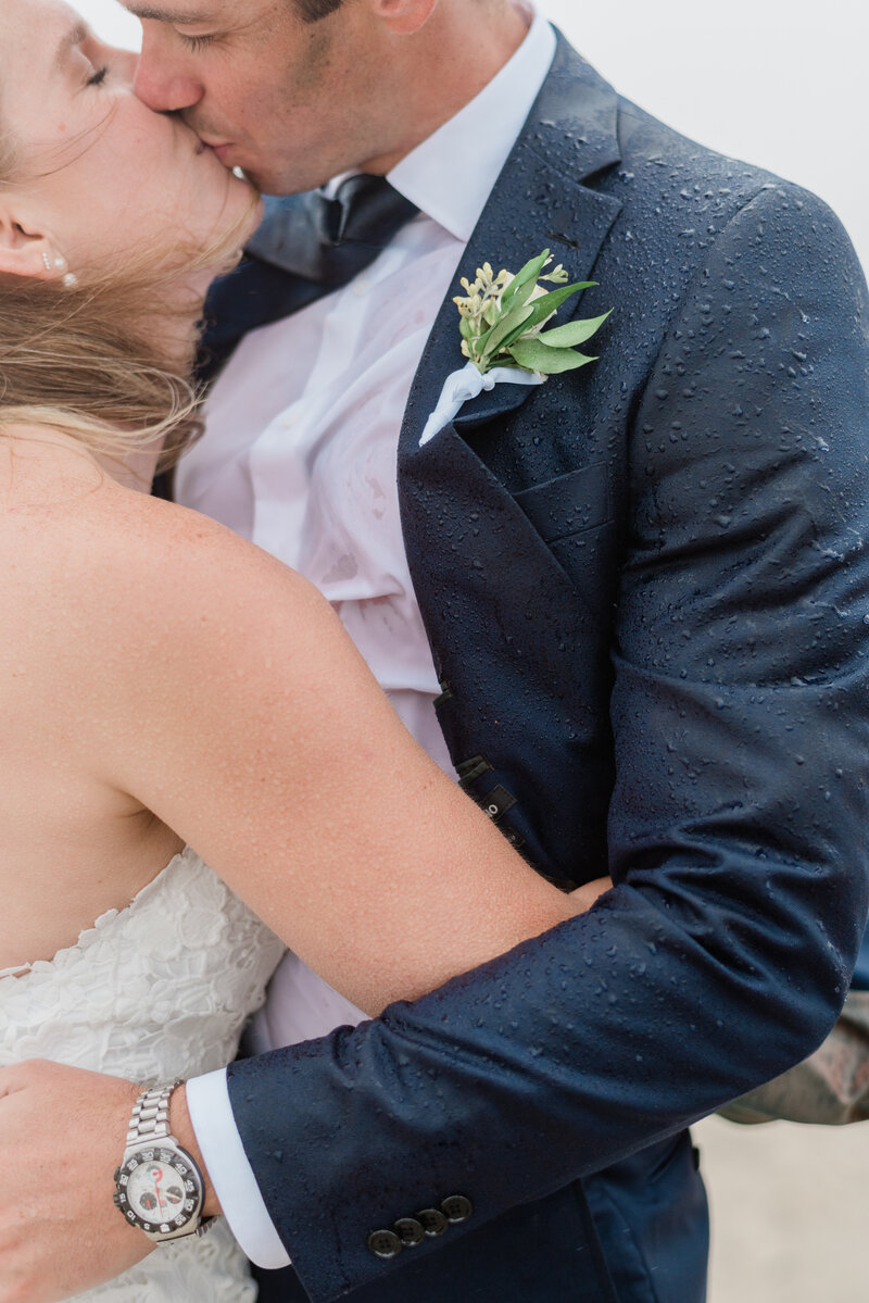 Newlyweds embrace in the rain while standing on the beach