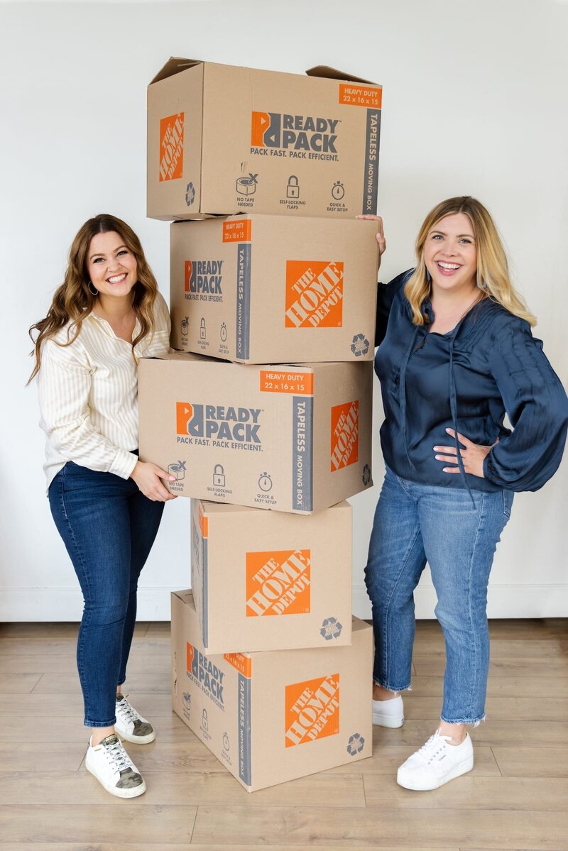 Keelie Luttrell and Brianna Castillo of Haven Realty Group smiling with moving boxes—representing their relocation concierge service helping clients move with confidence.