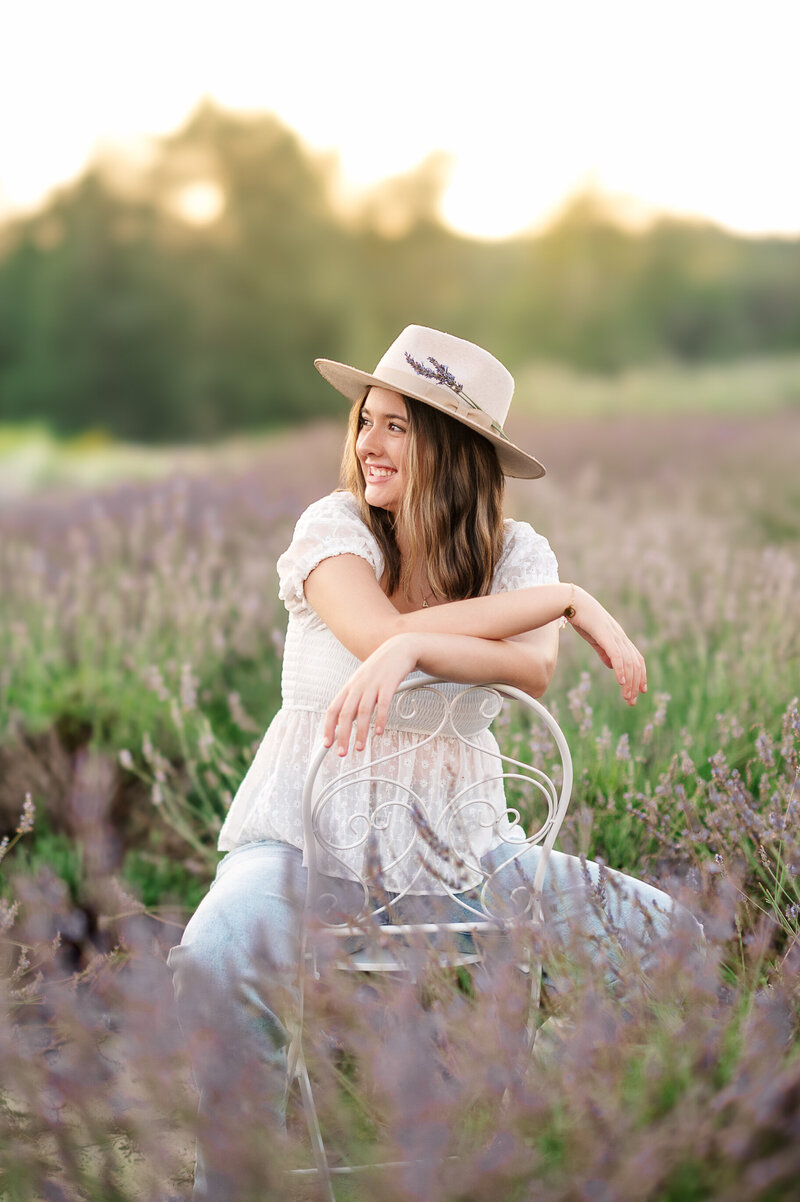 Young girl in a white shirt sitting on chair in a blooming lavender field during a senior session in Harrisburg, PA.