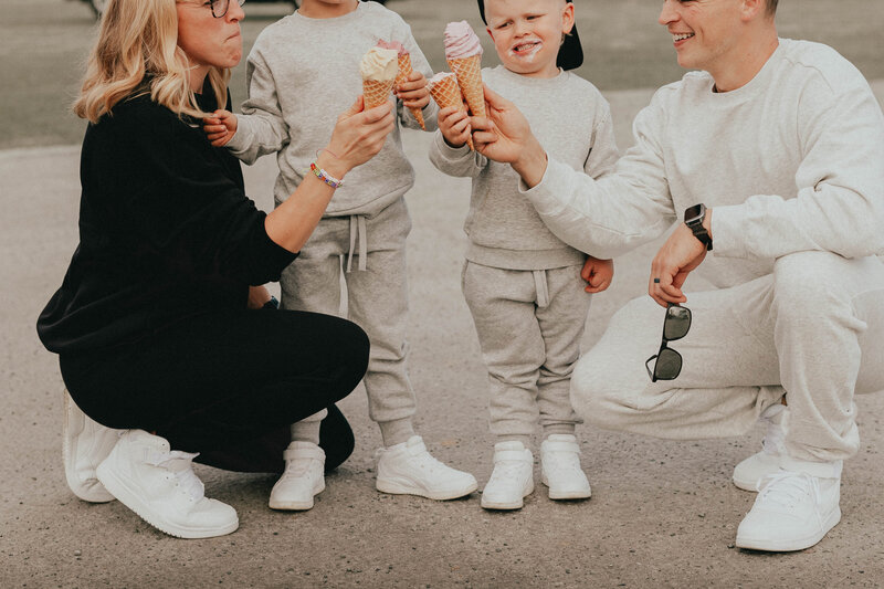 Photo of a family of 4, 2 parents and 2 young boys, wearing matching sweat suits and holding ice creams in a "cheers" position, taken by a langley photographer
