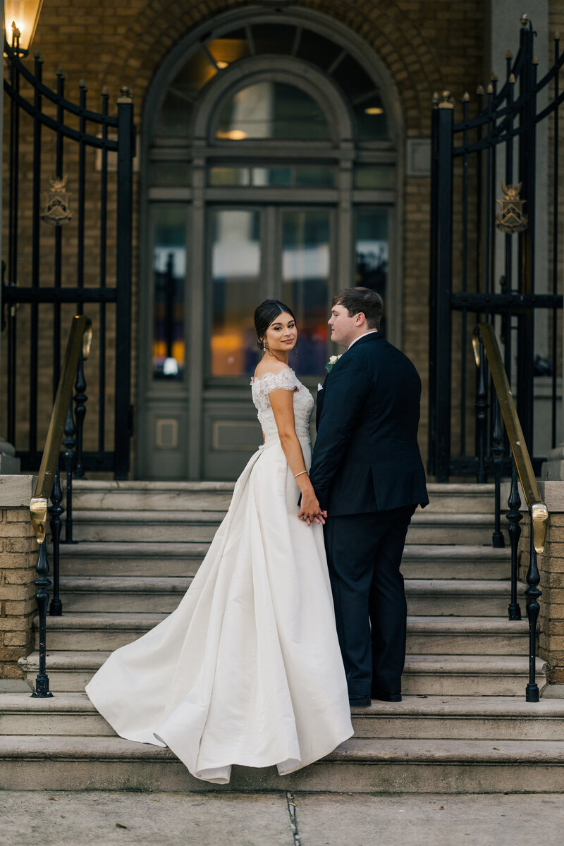 Bride standing gracefully as delicate details of her wedding gown are highlighted. A refined, intimate bridal moment captured in soft light
