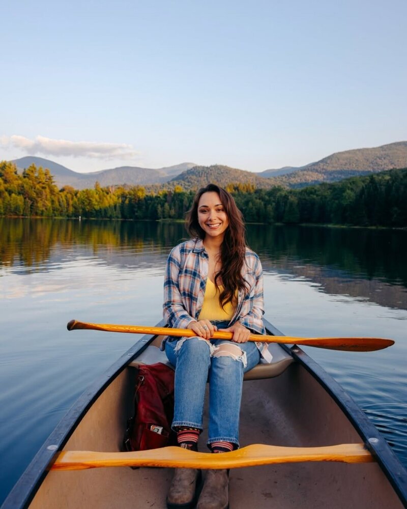 influencer jkrow sitting in a canoe on a sunny day in upstate new york wearing jeans and flannel