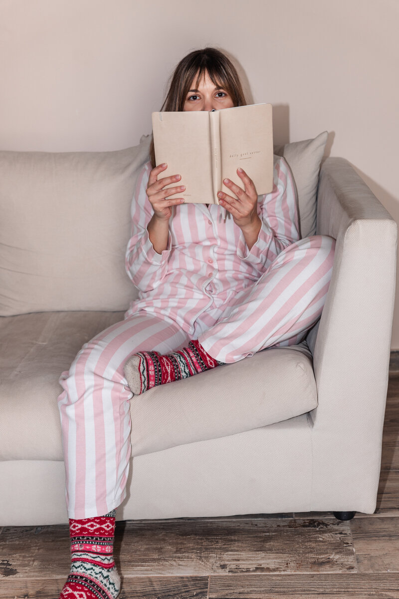 a girl sitting on the couch wearing her pink and white striped pajamas and colourful warm socks with a book in hand looking at the camera
