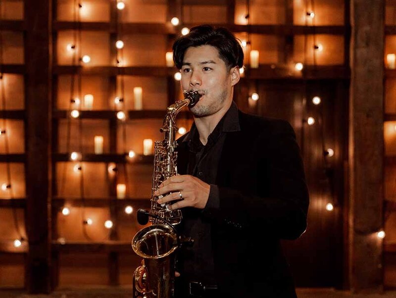 Saxophonist performing at an elegant indoor wedding with warm string lights and candles in the background.