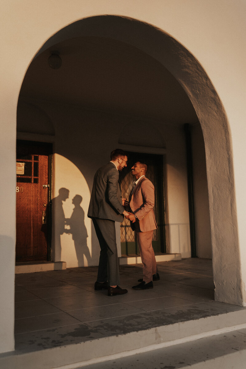A couple hold hands and share a quiet moment under the archway of a building, their shadows cast against the wall by the setting sun in Tucson, Arizona.
