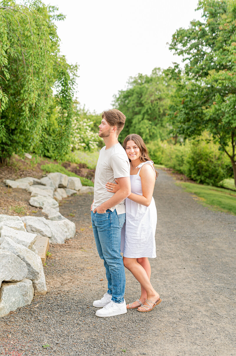 And engagement photo of a couple with her arms wrapped around him and smiling at the camera at a park in Moscow, Idaho