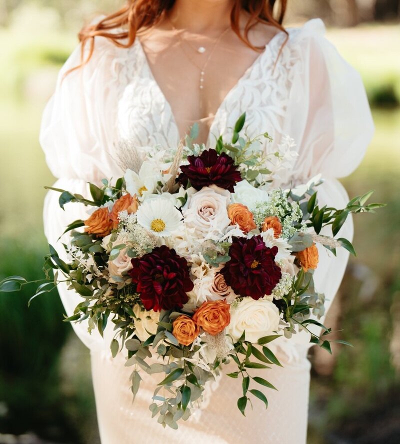 Bride holds her Yosemite Wedding bouquet with white, red, and orange flowers in front of her