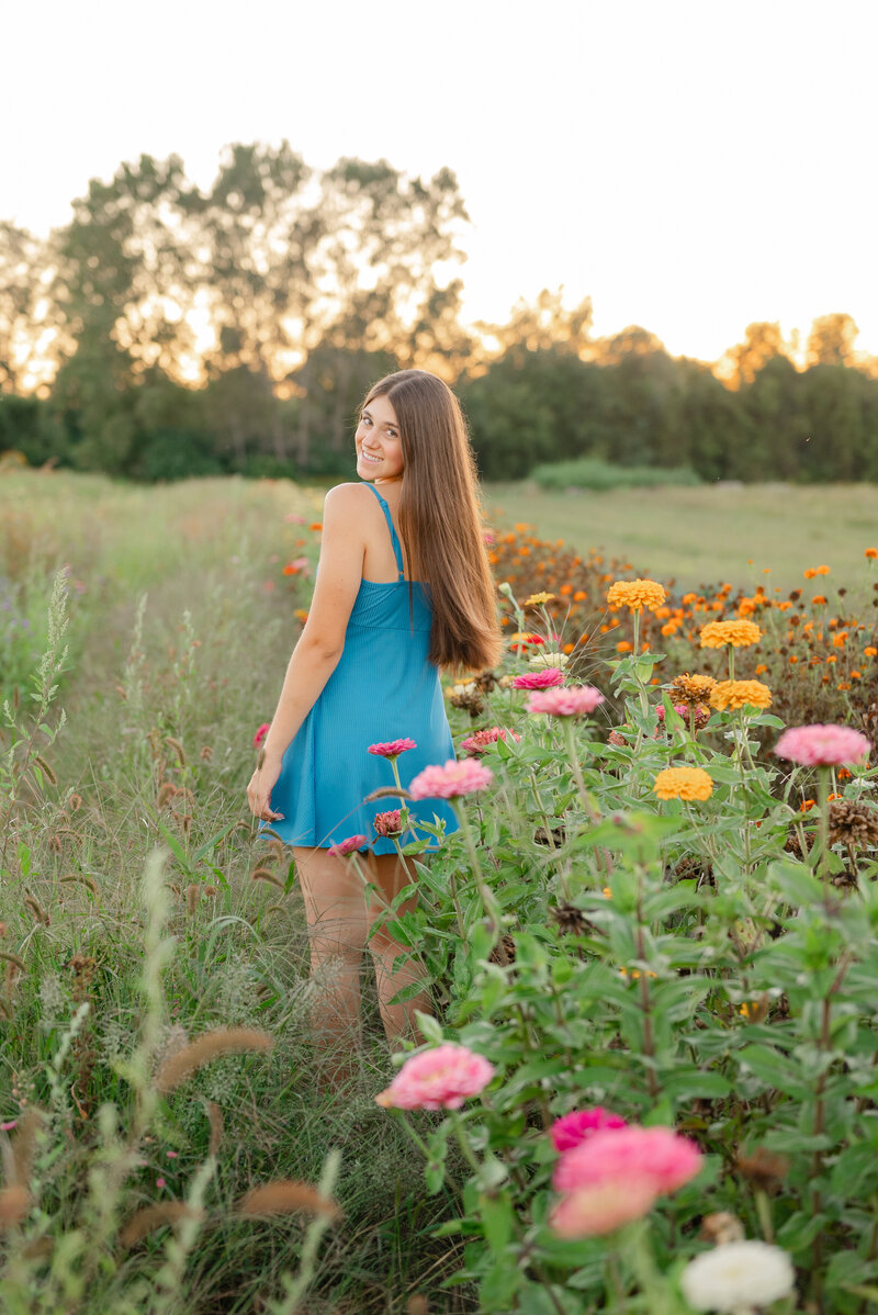 A high school senior girl standing in a flower field surrounded by a warm glow of the sun.