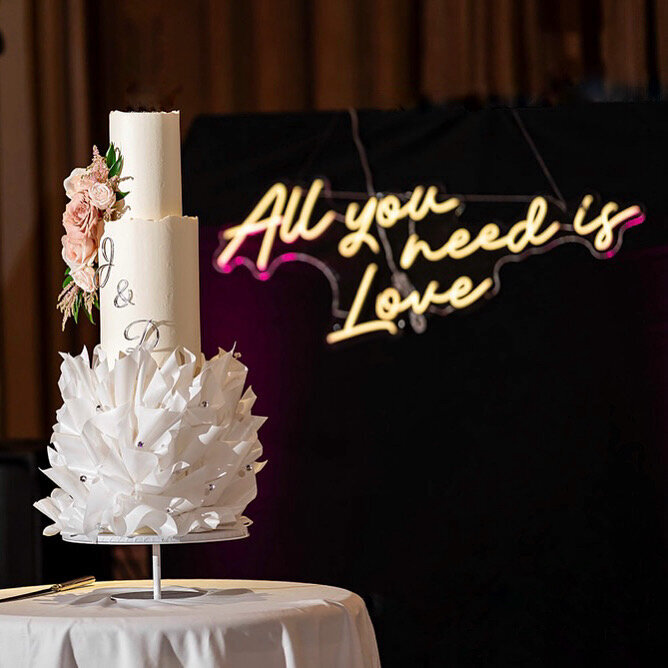 A bride on her wedding day in her wedding dress standing with her three tier wedding cake in  pink and white fresh florals at the Dog & Fox Wimbledon Village