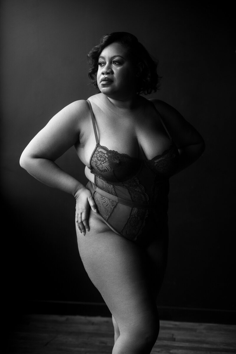 DC boudoir photographer Nicole Griffin stands in her studio in lace lingerie with a hand on her hip looking over her shoulder