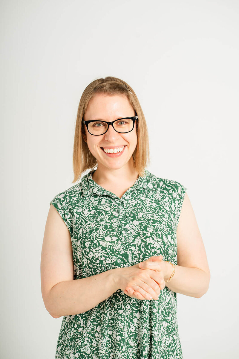 Stephanie clasps her hands in front of her while smiling at the camera.