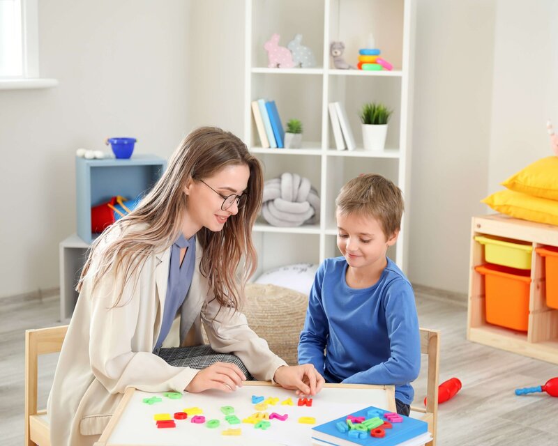 Speech-language pathologist working with a young boy on letter recognition during a therapy session in a bright, child-friendly room in Clinton, NJ.