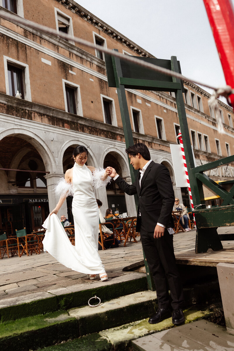 Bride and Groom on pier in Venice. Groom helps bride into the Gondola. 