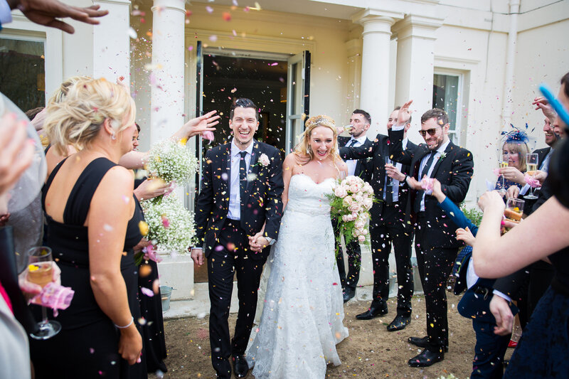 Bride and groom walking through confetti throw at their Surrey wedding
