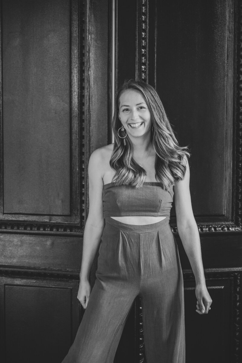 Katie smiles brightly at the camera in front of a dark wooden wall.
