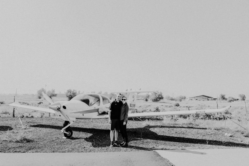 A black and white image of a young couple in front of a small, propeller plane