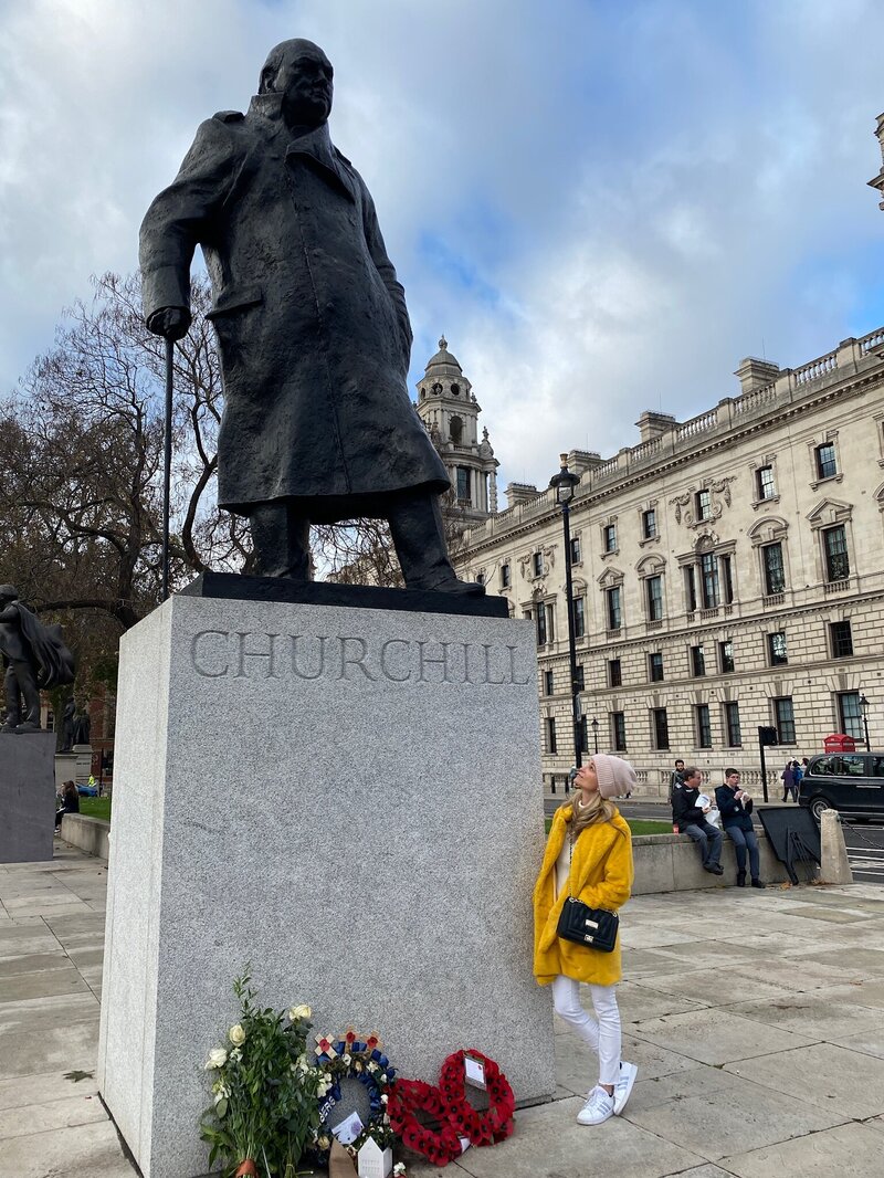 Woman in yellow fur coat gazes up at Winston Churchill Statue in Parliament Square, London, UK