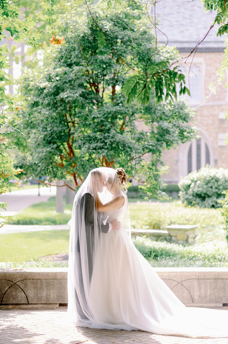 bride and groom embracing while wrapped in the veil
