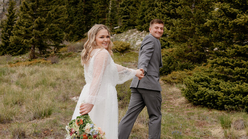 Couple in wedding attire holding hands and walking up a mountain