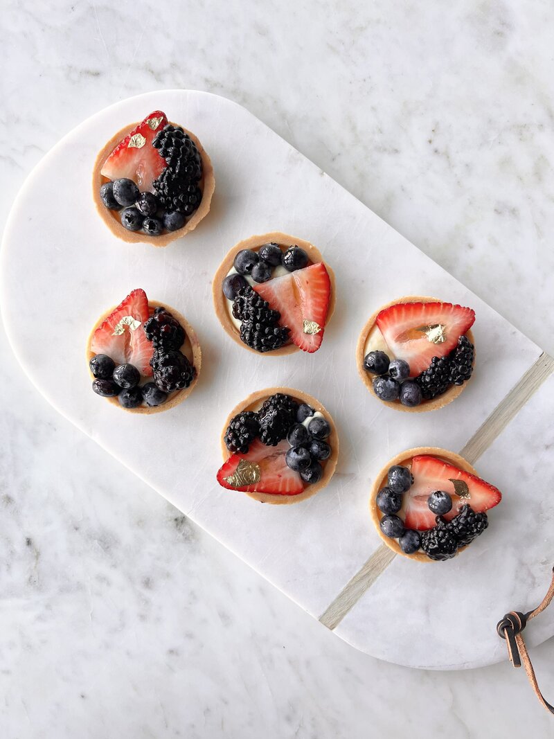 Vanilla custard and fresh fruit tarts on a marble platter and table