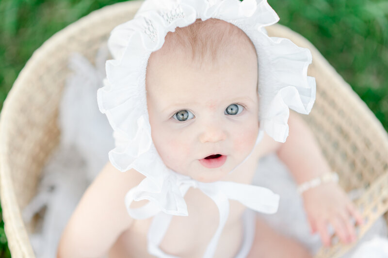 A 9 month old baby girl wears a white heirloom bonnet and bracelet by luxury newborn photographer kristie lloyd