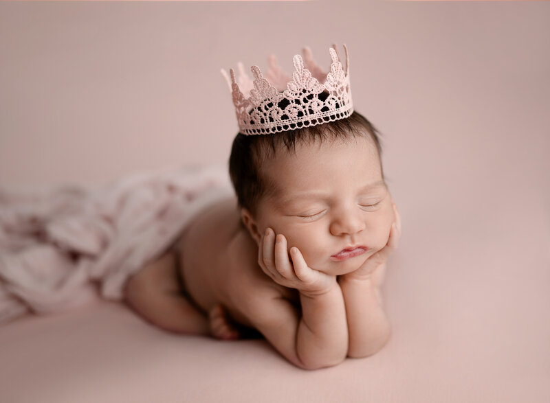 Baby girl on pink backdrop with pink grown on head. Sleeping with her hands under her chin. Photo taken by Jenni Nikki at Marietta Photo studio.