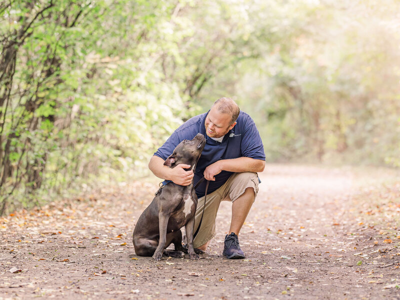 Matthew Lamarand kneeling on a trail in Plymouth, MI, getting kisses from a rescued grey pitbull named Adiela during training