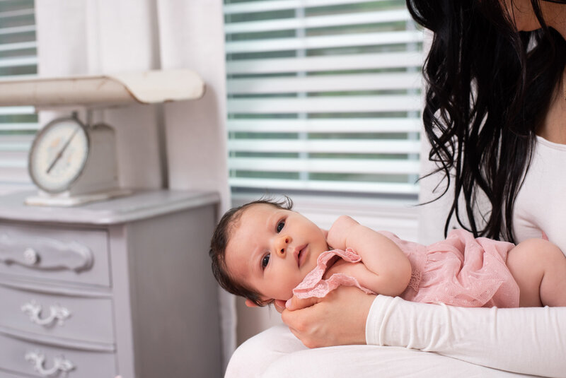 A newborn baby girl being held by her mom and in a pink dress.